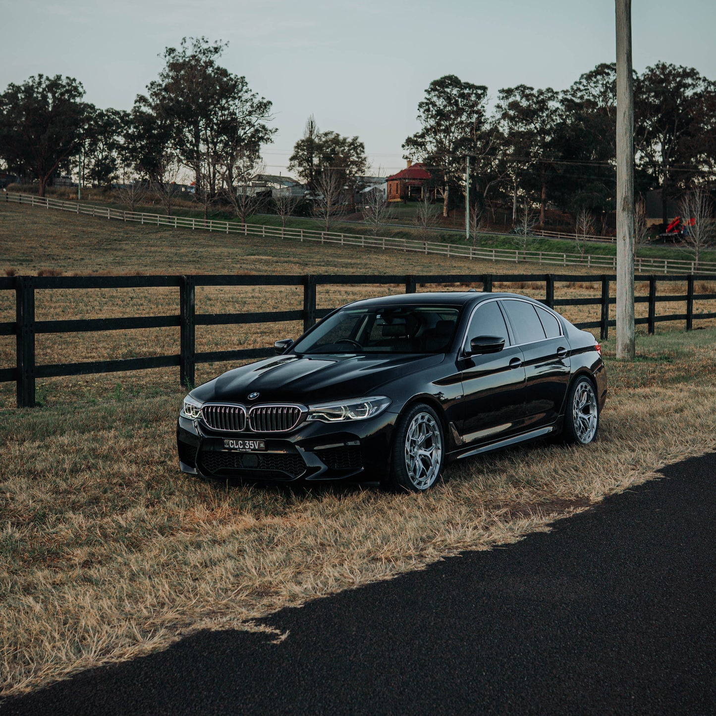 Black BMW car parked on a rural road with a wooden fence and trees in the background.
