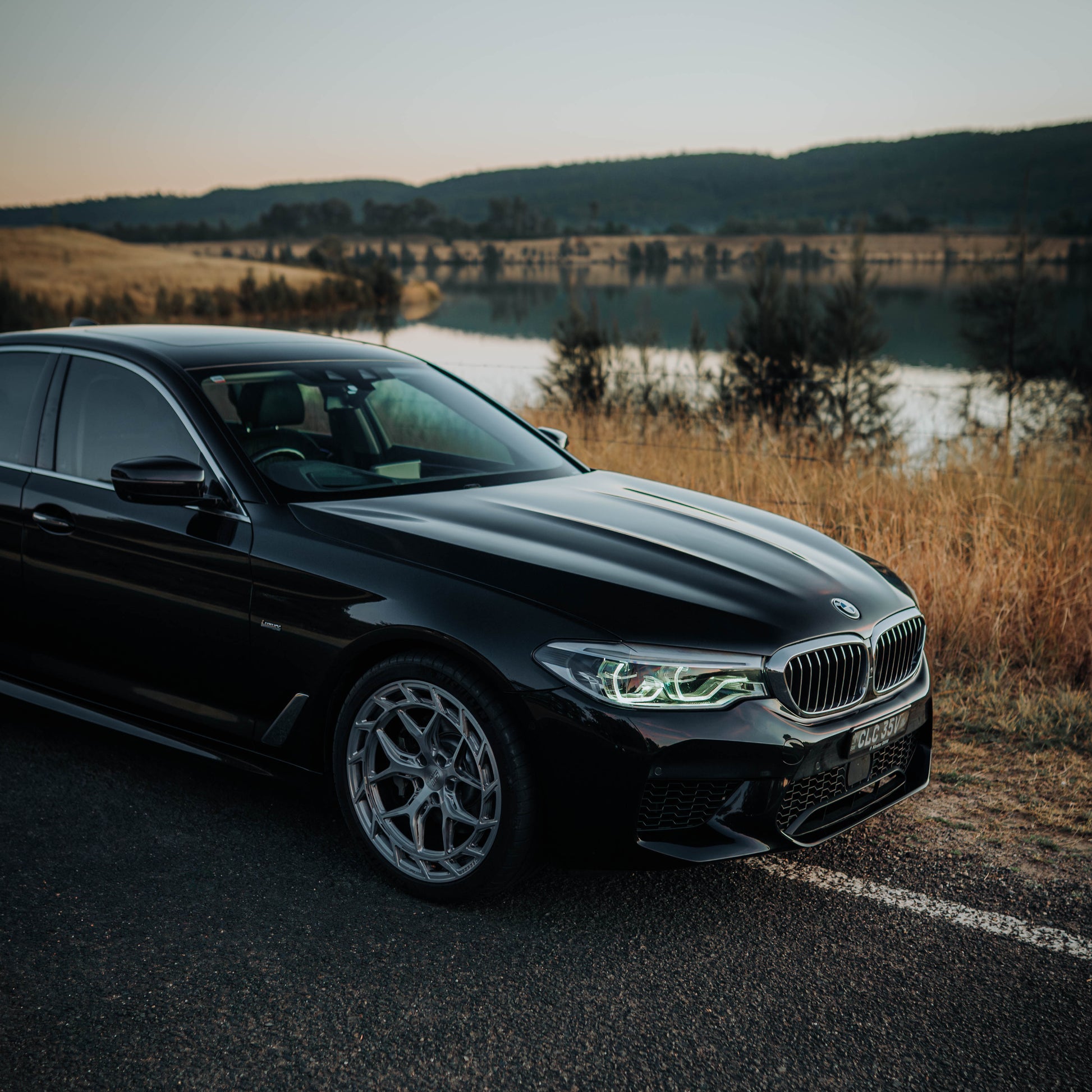 Black BMW car parked on a road with a scenic background of a lake and mountains.