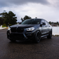 Black BMW car on a road with a cloudy sky and trees in the background