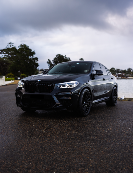 Black BMW car on a road with a cloudy sky and trees in the background