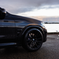 Black car parked by a body of water with a cloudy sky.