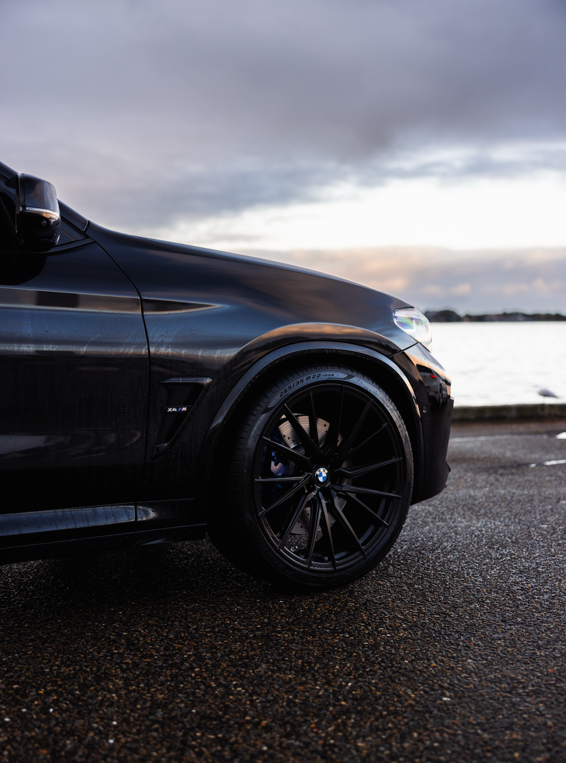 Black car parked by a body of water with a cloudy sky.